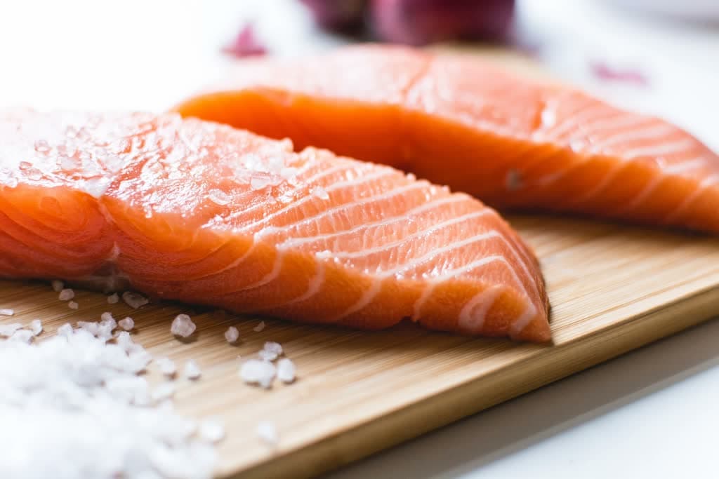 Raw salmon fillet on a cutting board with salt.
